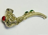 Front view showing detailed dragon carving around the bowl of the pipe with a red stone on the side and green stones on the curved stem.
