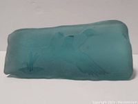 Side view of blue-green frosted glass paperweight featuring etched flying duck near grass or reeds