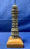 Full view of the vintage Asian metal pagoda statue on wooden base showing intricate tiered architectural details and structure.