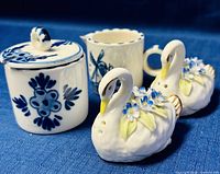 Front view of miniature Delft sugar bowl with lid, creamer with windmill design, and the pair of Royal Adderley floral swan salt and pepper shakers on blue fabric background