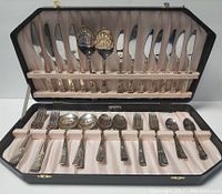 Photo of the flatware set arranged inside the storage case showing knives in upper area and forks, spoons, and serving utensils in lower area.