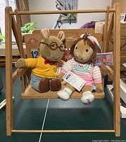 Arthur and D.W. plush characters seated on the wooden toy swing with tags attached