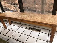 Solid wood bench on tiled floor near window with visible wear on top surface and legs