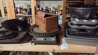 Cast iron pans, tart pans, muffin tins, and other bakeware stacked and arranged on shelving with some packaging boxes visible.