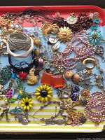 Full lot of costume jewelry on a striped tray showing various styles and colors including sunflower pins and beaded necklaces.