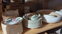 Photo showing stacked plates, bowls, and covered dish arranged on shelving in basement. Includes protective cases for some items.