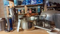 Aluminum mixing bowl, copper mixing bowl, and other kitchen utensils on wooden shelving in basement storage area.