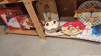 Photo of various Christmas themed serving dishes and plates including Santa platter, Christmas tree dish, gingerbread boy bowl, snowman plate, and other colorful holiday party plates arranged on shelves.