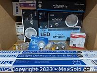 Photo showing assorted unopened packaged lightbulbs including Philips daylight deluxe tubes, Cree Enhance LED bulbs, TCP daylight LED 10-pack, a Satco incandescent bulb, and Cree LED recessed light trims.