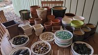Wide view of table showing multiple clay and glazed flowerpots, decorated pots, and containers of decorative stones and marbles grouped together
