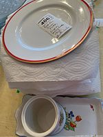 Eighteen white serving plates with red trim and gold edge stacked.