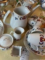Photo showing coffee pot, water pitcher, creamer, sugar bowl with lid, cups and plates arranged on a table, displaying colorful floral patterns and gold trim.