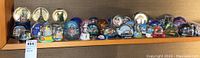 Wide shot showing over two dozen snow globes arranged on shelf, various sizes and themed designs featuring city landmarks