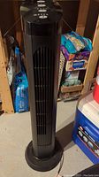 Full height view of the black plastic Cascade tower fan standing on floor, showing front grille and base.