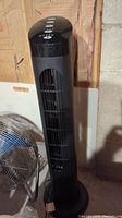 Full tower fan showing tall black design with vertical grille and circular base.