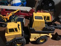 Wide shot showing multiple large vintage metal toy trucks including a yellow Tonka diesel truck and heavy duty towing truck with black rubber tires, a red fire department truck, and a blue and white cement mixer truck.