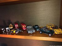 Multiple metal toy vehicles displayed on a shelf, including motorcycles, London buses, and sports cars under warm lighting.