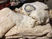 Photo of stacked vintage hand crochet and embroidered linens on a table showing detailed crochet patterns and lace textures.
