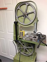 Front view of green metal bandsaw showing upper and lower guide wheels, support column, work table and base