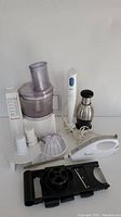 Wide photo showing Moulinex food processor with attachments, Braun hand blender, PC food chopper, and Toastmaster electronic carver on white background.