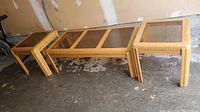 Photo showing wooden coffee table with three rectangular glass panels and two matching end tables with square glass tops on concrete floor.