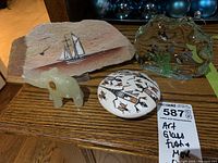 Photo showing the glass fish scene sculpture, painted stone with sailing ship, painted stone with lizards and insects, and onyx elephant figurine all arranged on wooden surface.