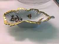 Side view of oval scalloped porcelain bowl, white with gold trim and bird and butterfly hand painted decoration