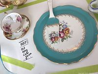 Photo showing the Old Foley cake server plate with floral design, turquoise border, and the Staffordshire teacup placed beside it.