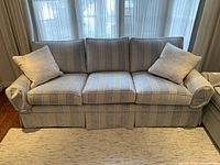 Front view of three-seat striped upholstered sofa with two throw pillows in front of window