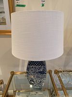 Full view of table lamp showing white fabric shade and porcelain base with floral and bird design.