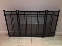 Full view of the black cast metal three-panel fireplace screen featuring a geometric design and mesh center.