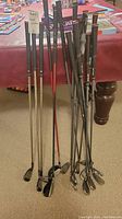 Full overview of ten right-handed golf clubs, including woods and irons leaning against sofa