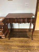 Front view of the wood hall table showing the table top, drawer, and curved legs with brass handles.