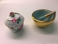 View of both items in the set: lidded pot with floral rose design and sculpted rosebud top, and the gold and turquoise mortar and pestle.