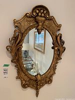 Front view of the gilded oval mirror showing ornate floral and leaf carvings on the wood frame.