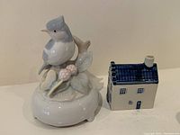 Front view of porcelain bird music box and KLM house side by side on a flat surface.
