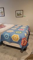 Twin bed covered with blue quilt decorated with various hexagonal floral patchwork patterns in multiple colors.