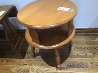 Side view of round wood side table showing two levels and turned legs on wood flooring.