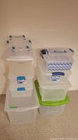 Stack of clear plastic bins of varying sizes, blue latch handles on several, green lid at base