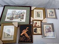 Eight assorted framed artwork pieces laid out showing diversity in sizes, frames, and styles.