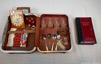 Open suitcase bar kit showing glasses, spoons, Viking bottle stoppers, towel, and wooden sign.