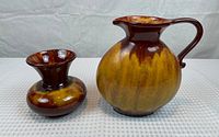 Photo showing Blue Mountain Pottery pitcher and vase side by side on a white textured surface, highlighting the glaze pattern.