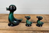 Set of three ceramic ducks by Blue Mountain Pottery, displayed on a wooden surface against a white background, showing general size difference and condition.