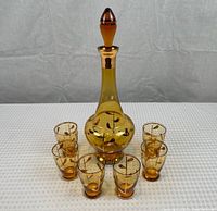 Full set showing one decanter with stopper surrounded by six matching glasses, all on a white textured surface.