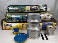 Camping lot showing three packed tents and camp cooking set including pots, cups, and plates.