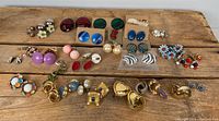 Top-down view of a variety of costume jewelry earrings arranged on a wood surface, showing a range of colors and styles including stud and clip-on earrings.