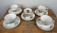 Top view of lot showing five tea cups and saucers with various floral designs and gold trims on wooden table.
