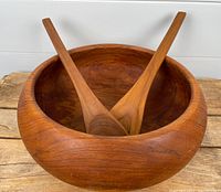 Front angled view showing the round teak salad bowl with two long wooden salad spoons inside.