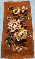 Full view of the rectangular hooked rug showing floral pattern against a brown background.
