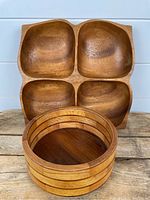 Photo showing the round wood bowl stacked in front of the square divided serving tray with four compartments.